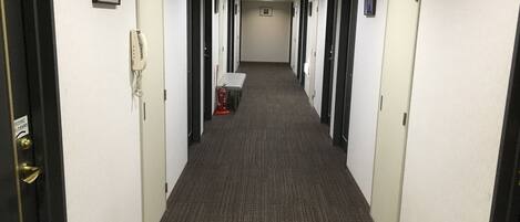 A hotel hallway with multiple doors, a fire extinguisher, and a bench.