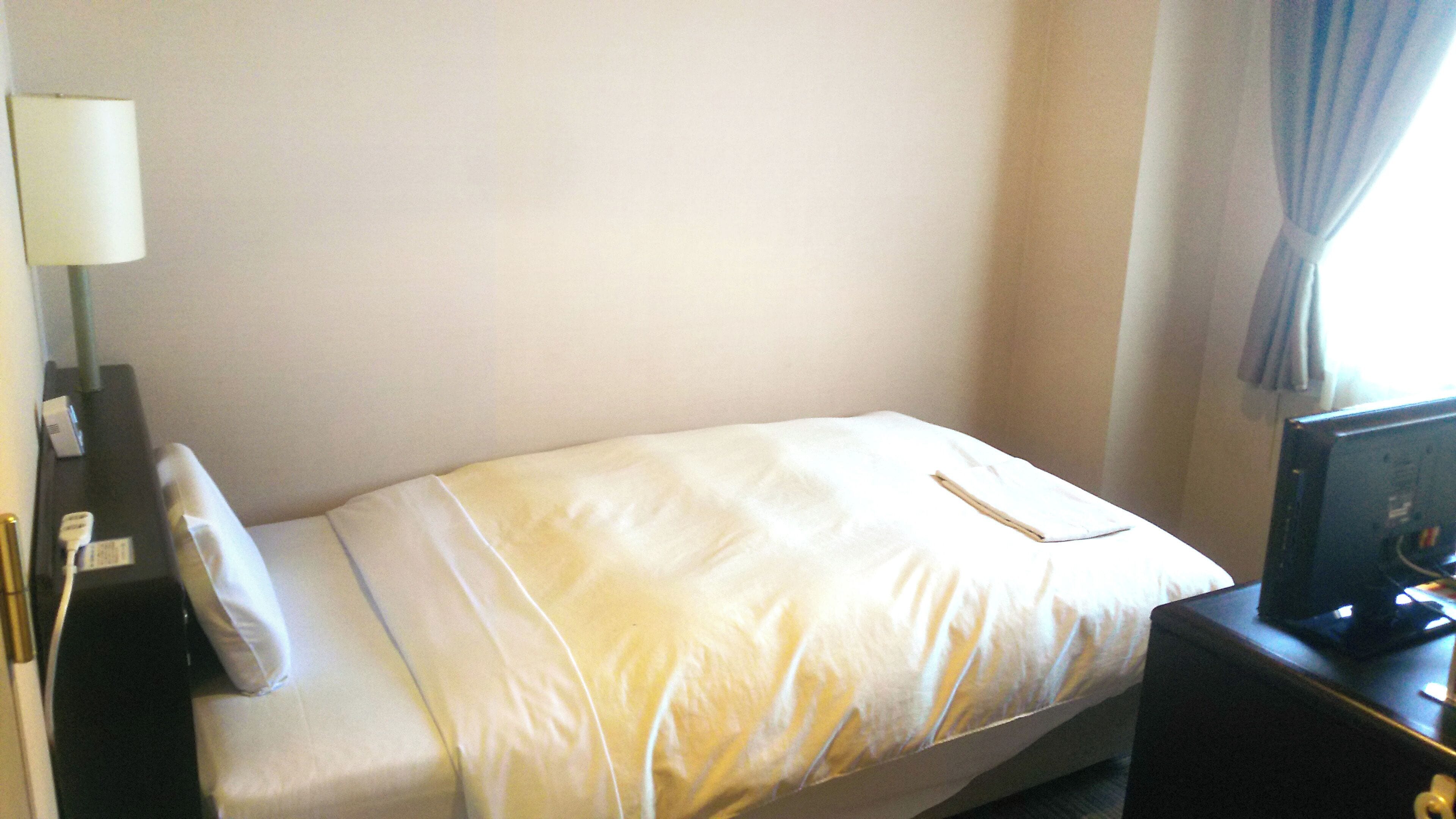 A hotel room with a bed, a nightstand, a lamp, and a television.