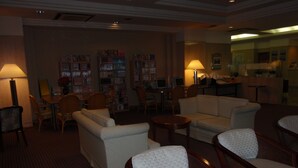 A hotel lobby with seating areas, a reception desk, and a bookshelf filled with books. - Hotel Crown Hills Okaya (Okaya)
