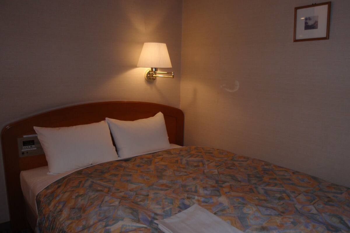 Ein Hotelzimmer mit einem Bett, einer Wandlampe und einem kleinen Bild an der Wand.