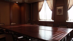 A conference room with a long table and chairs, large windows with curtains, and a framed picture on the wall. - Hotel Crown Hills Okaya (Okaya)