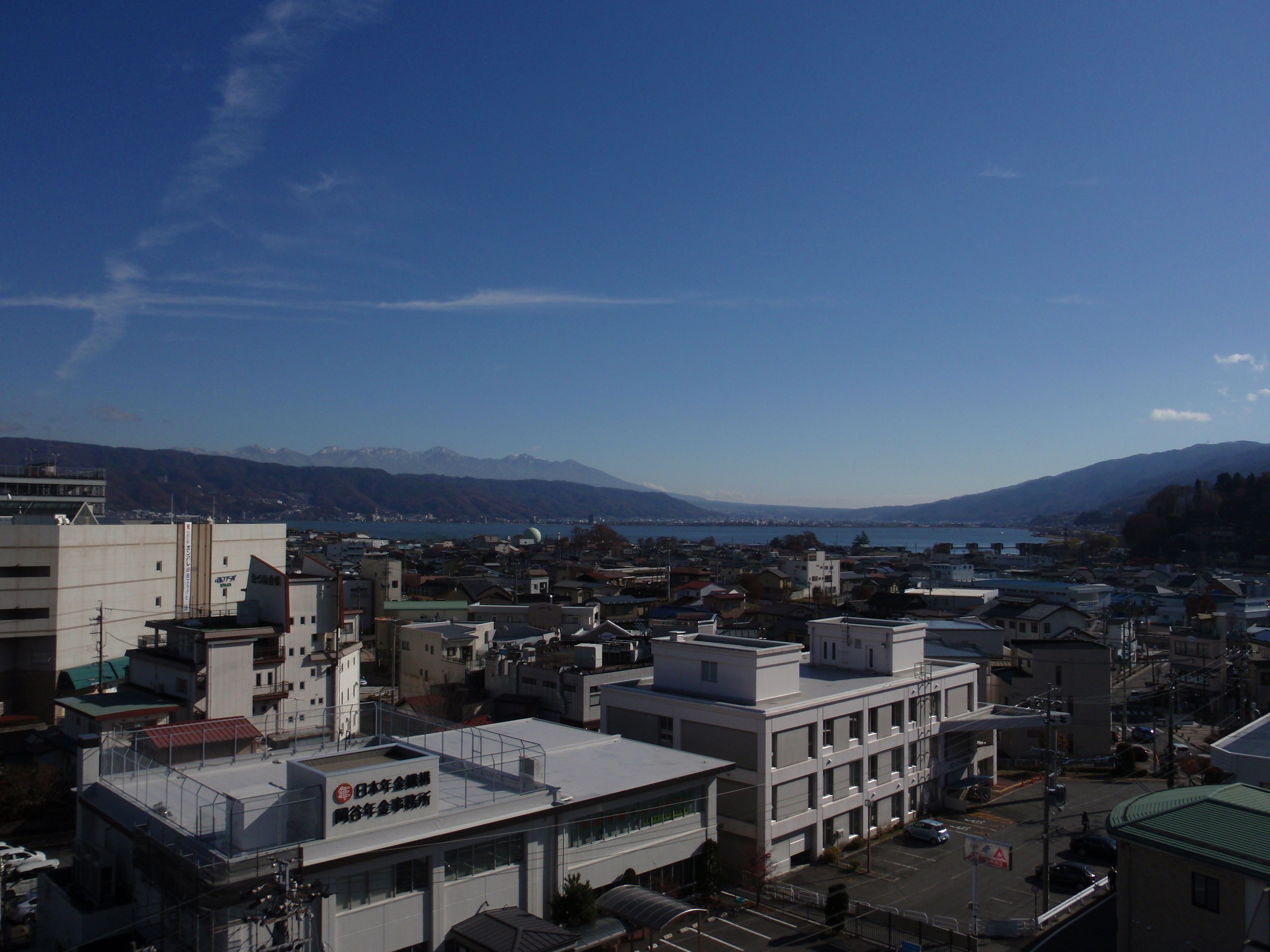 A cityscape with a mix of modern and traditional buildings, a clear sky, and a distant view of mountains and a body of water.