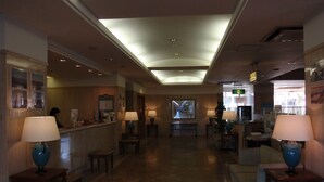 A hotel lobby with a reception desk, seating areas, and a view of the street through the glass wall. - Hotel Crown Hills Okaya (Okaya)