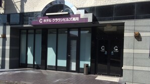 A hotel entrance with a sign in Japanese, large glass doors, and a trash bin outside. - Hotel Crown Hills Takaoka (Takaoka)