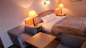 A hotel room with a bed, two armchairs, a small table, and two bedside lamps. - Hotel Crown Hills Takaoka (Takaoka)