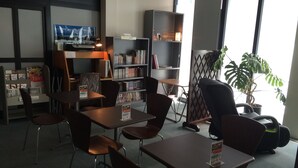 A library with tables and chairs, bookshelves, a television, and a potted plant. - Hotel Crown Hills Takaoka (Takaoka)