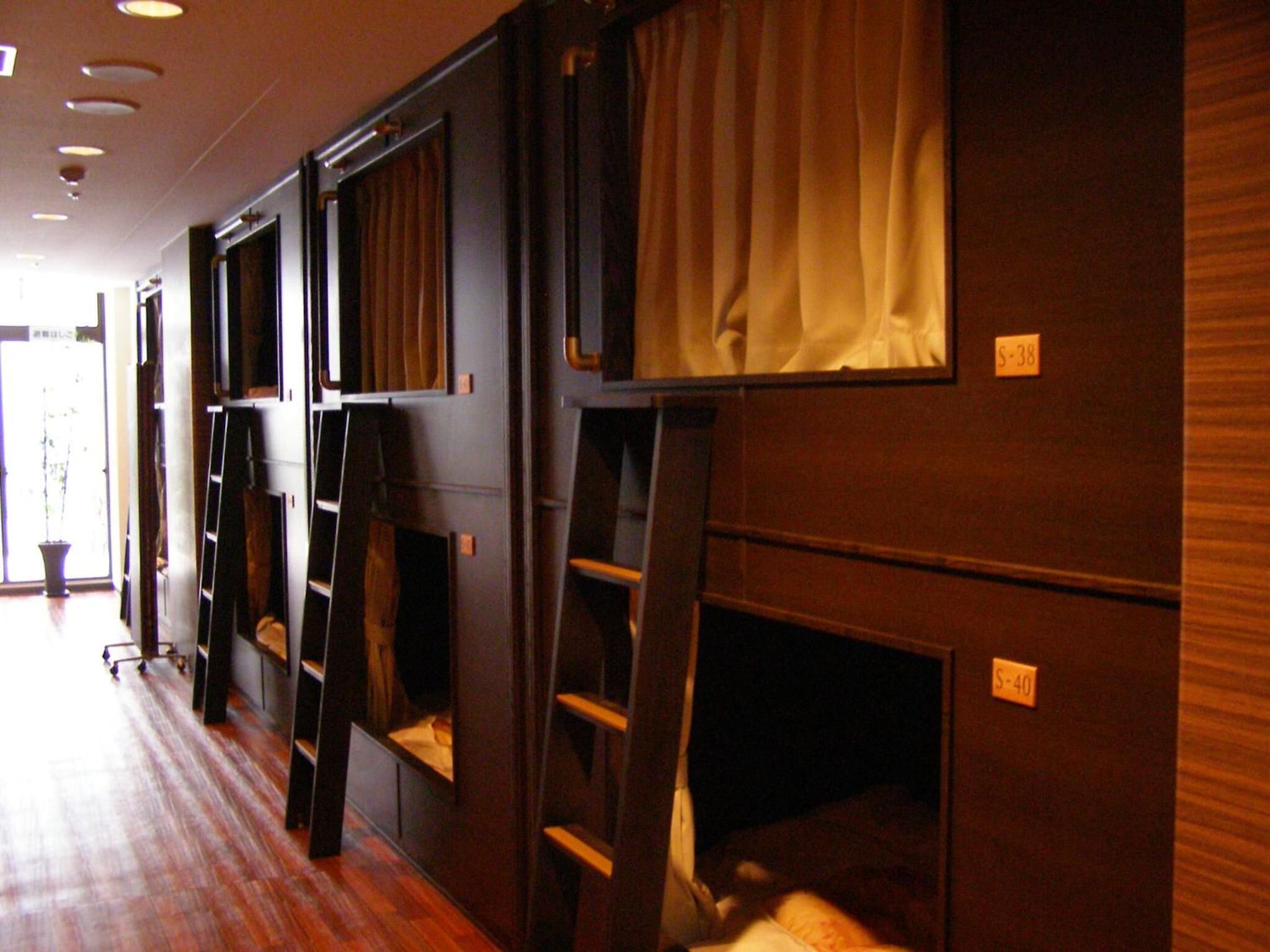 A row of bunk beds with attached desks and shelves, numbered room signs, and a wooden floor.