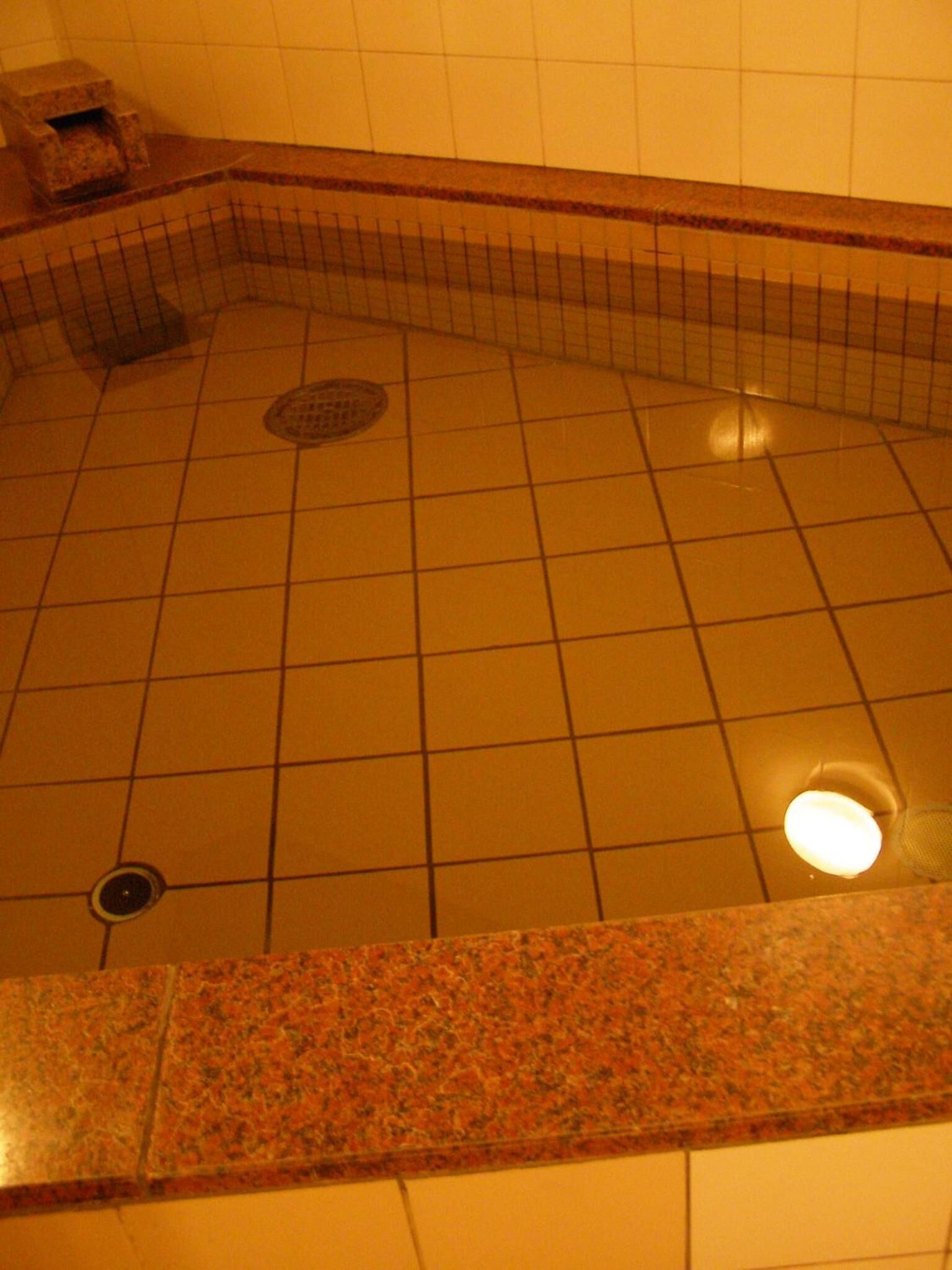 A tiled hot tub with a drain and a light fixture above it.