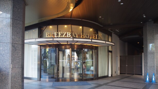The entrance of the Breezbay Hotel with a glass facade and a curved entrance. - Resort Capsule Sakuragicho (Yokohama)