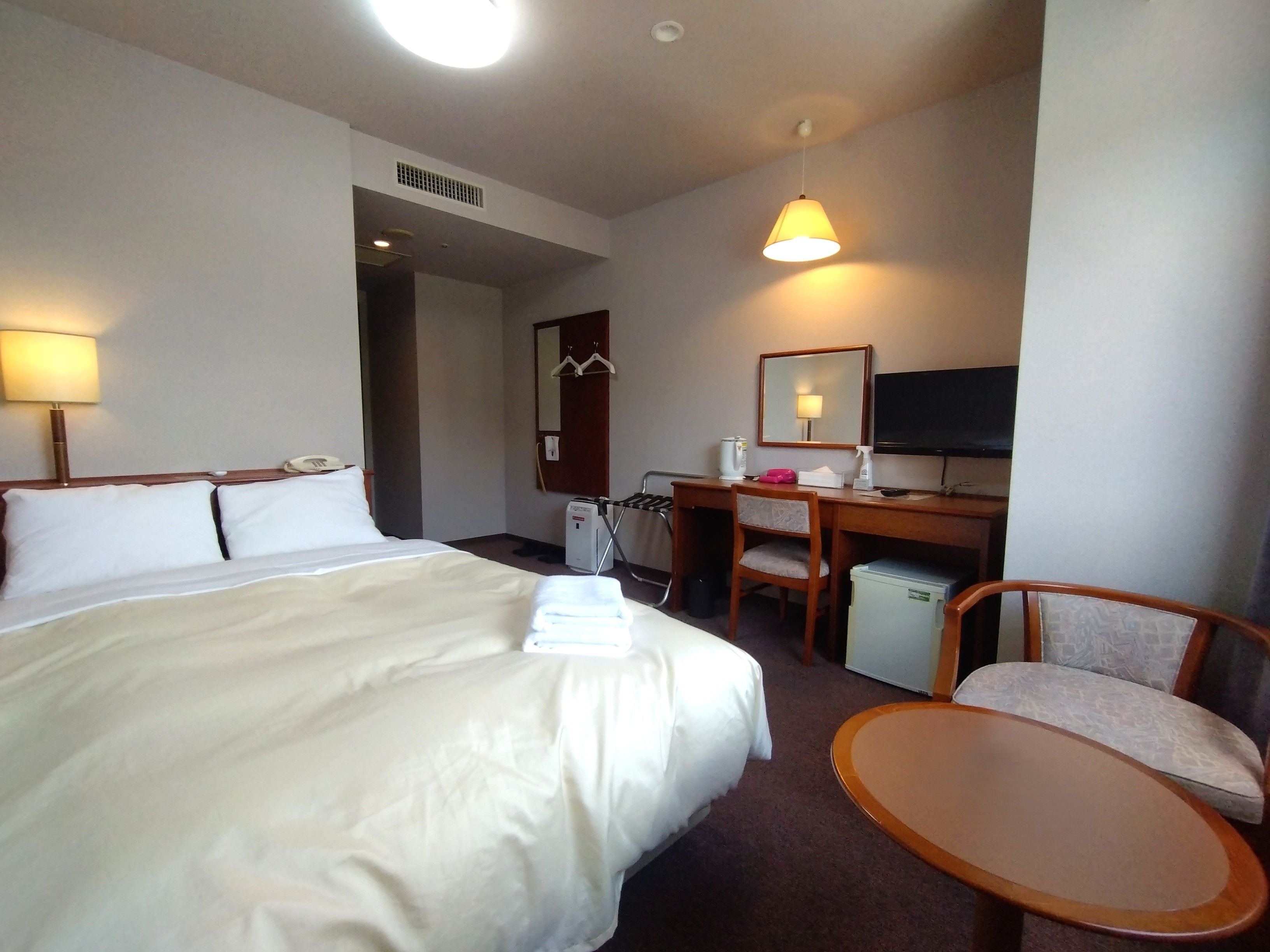 A hotel room with a bed, desk, chair, and a television.