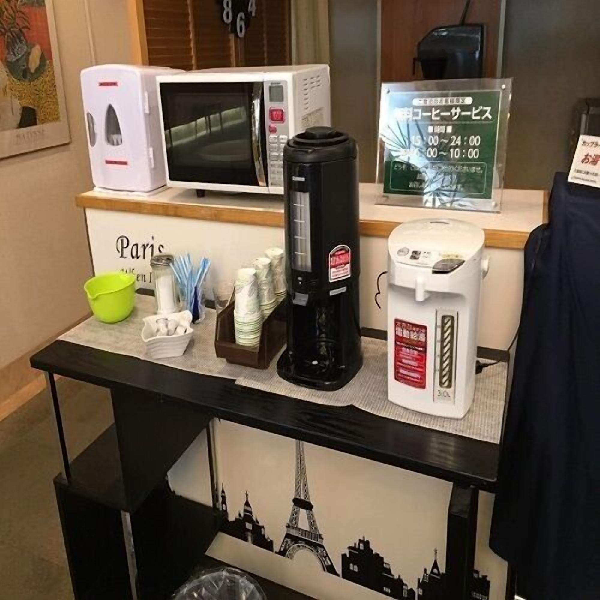 A coffee station with a coffee maker, cups, and a sign indicating service hours.