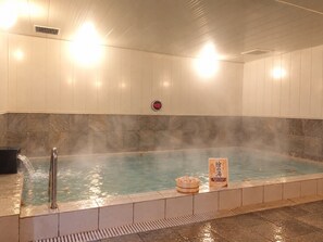 Baño de aguas termales con un temporizador digital, vapor elevándose del agua y un cartel que indica la temperatura.