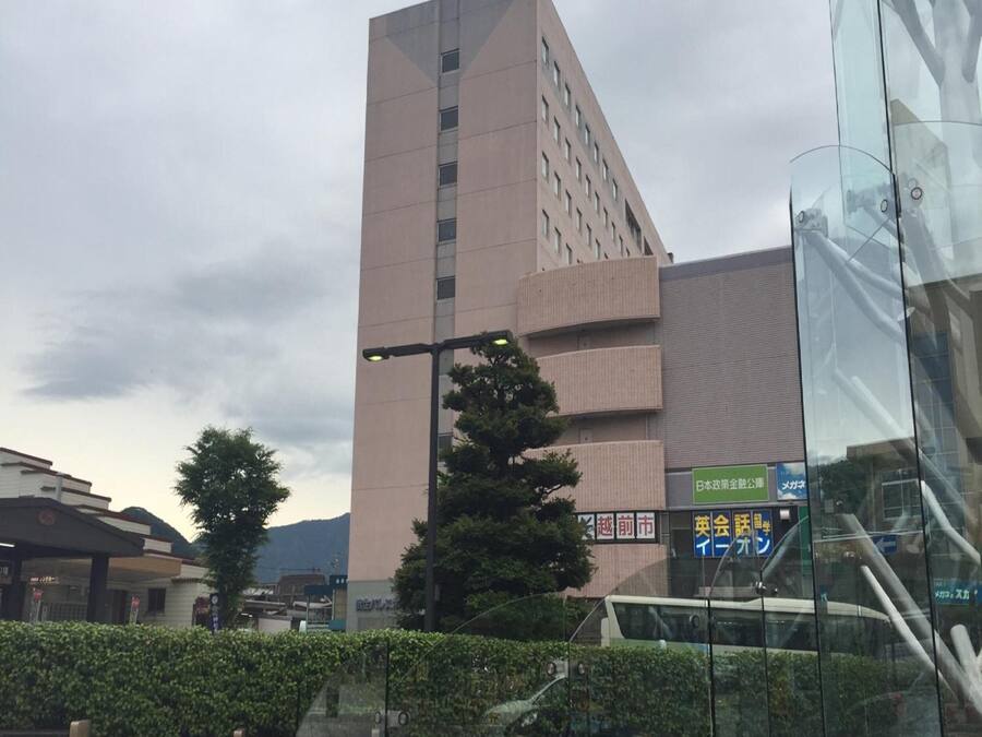 A modern building with a unique angular design, surrounded by greenery and a clear sky.