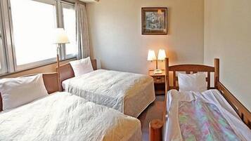 Quarto de hotel com duas camas de solteiro, mesa de cabeceira com luminárias, um quadro na parede e janela com cortinas.