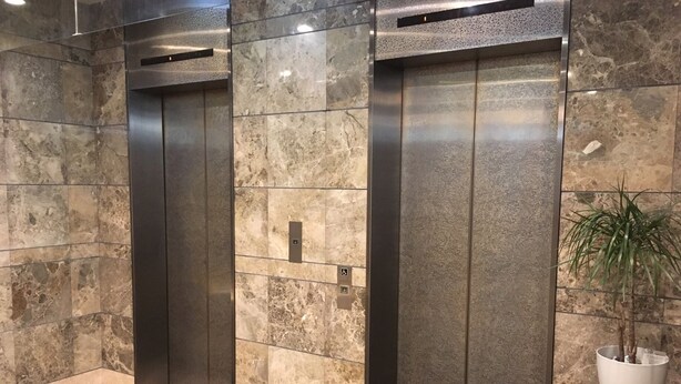 Two elevator doors in a lobby with marble walls and a potted plant. - Hotel Crown Hills Takefu (Echizen)