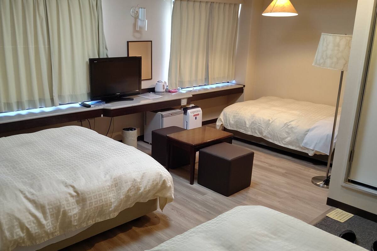 Une chambre d’hôtel avec deux lits, un bureau avec un ordinateur, une petite table et une lampe.