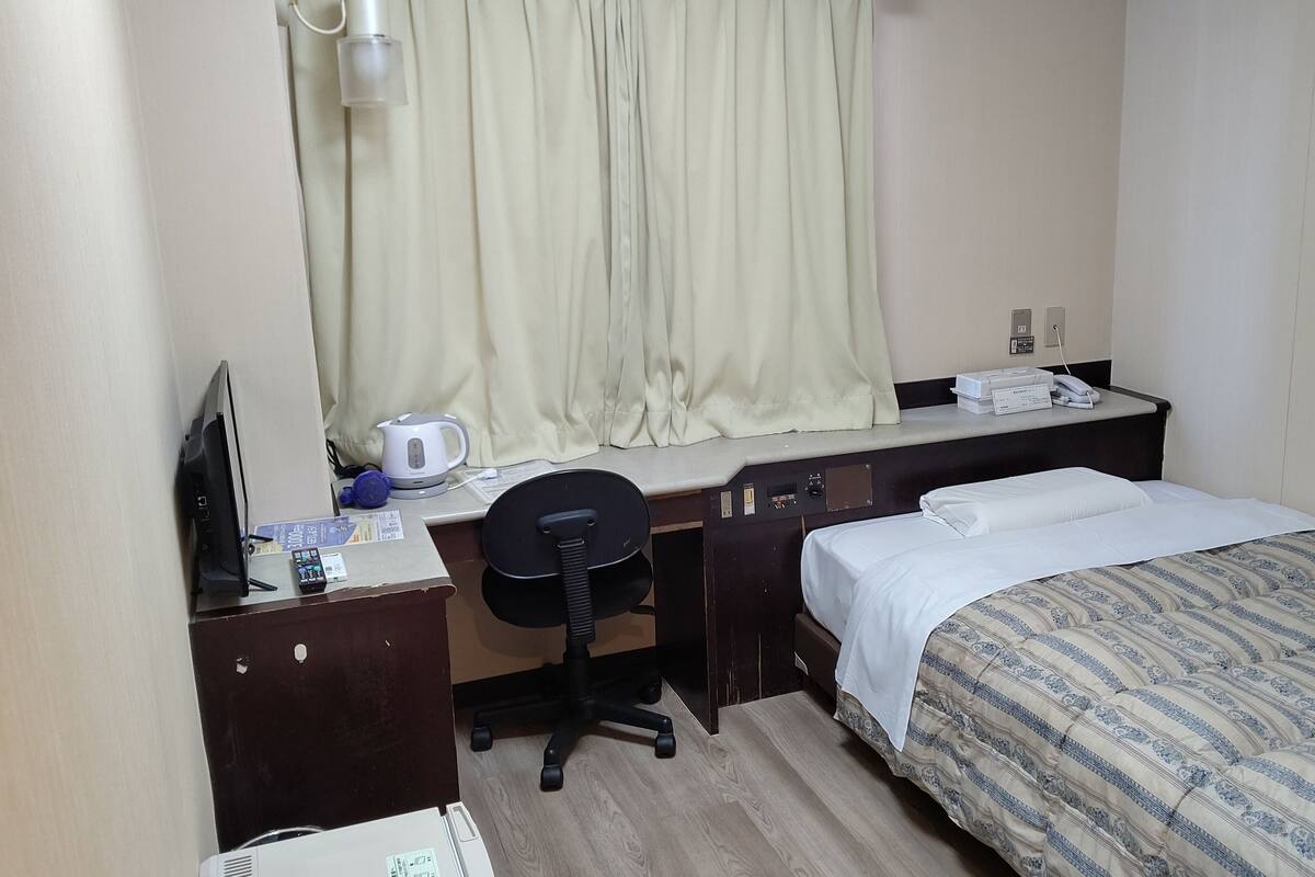 Une chambre d’hôtel équipée d’un lit, d’un bureau avec un ordinateur, d’une chaise, d’une bouilloire et d’un téléphone.
