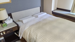 Una habitación de hotel con una cama, una mesita de noche con una lámpara, un reloj y una caja de pañuelos.
