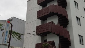 Un edificio moderno con un diseño espiral único para su escalera, un letrero que dice 'Ishima Central Hotel Townhouse', y un área de entrada techada.
