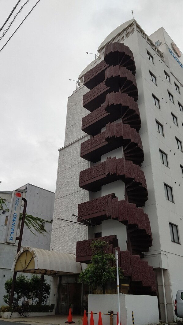 A modern building with a unique spiral staircase design, a sign for 'Ishima Central Hotel Townhouse', and a covered entrance area.