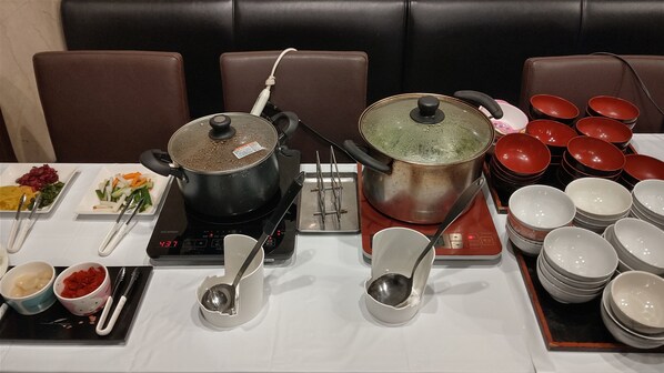A dining table set with multiple pots, bowls, and utensils, indicating a meal setup in a restaurant or dining area. - Tsuyama Central Hotel Town House (Tsuyama)