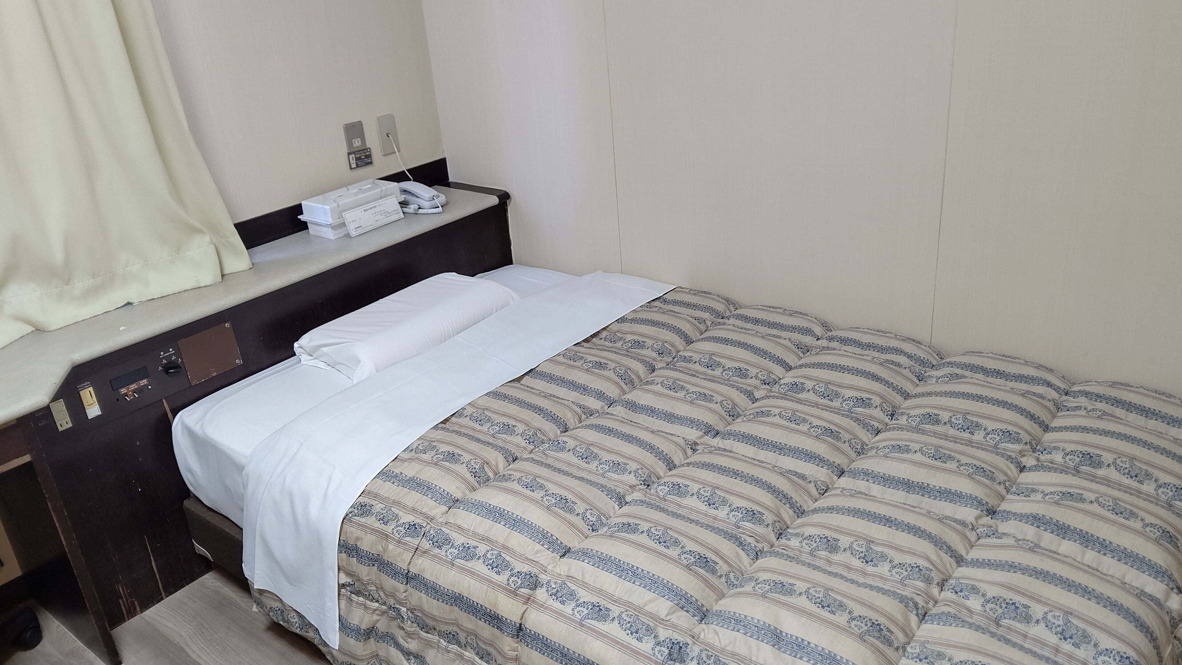 A hotel room with a bed, a desk with a telephone, and a small table with a lamp.