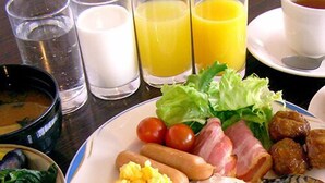 A breakfast plate with eggs, sausages, bacon, tomatoes, lettuce, and a side of rice.