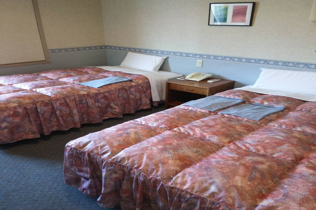 A hotel room with two beds, each with floral-patterned bedding, a bedside table with a phone, and a small wall-mounted picture.