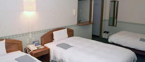 A hotel room with two single beds, a bedside table with a lamp, a mirror, and a small window.