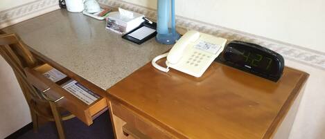 A hotel desk with a telephone, a digital clock, a tissue box, a pen, and a notepad.