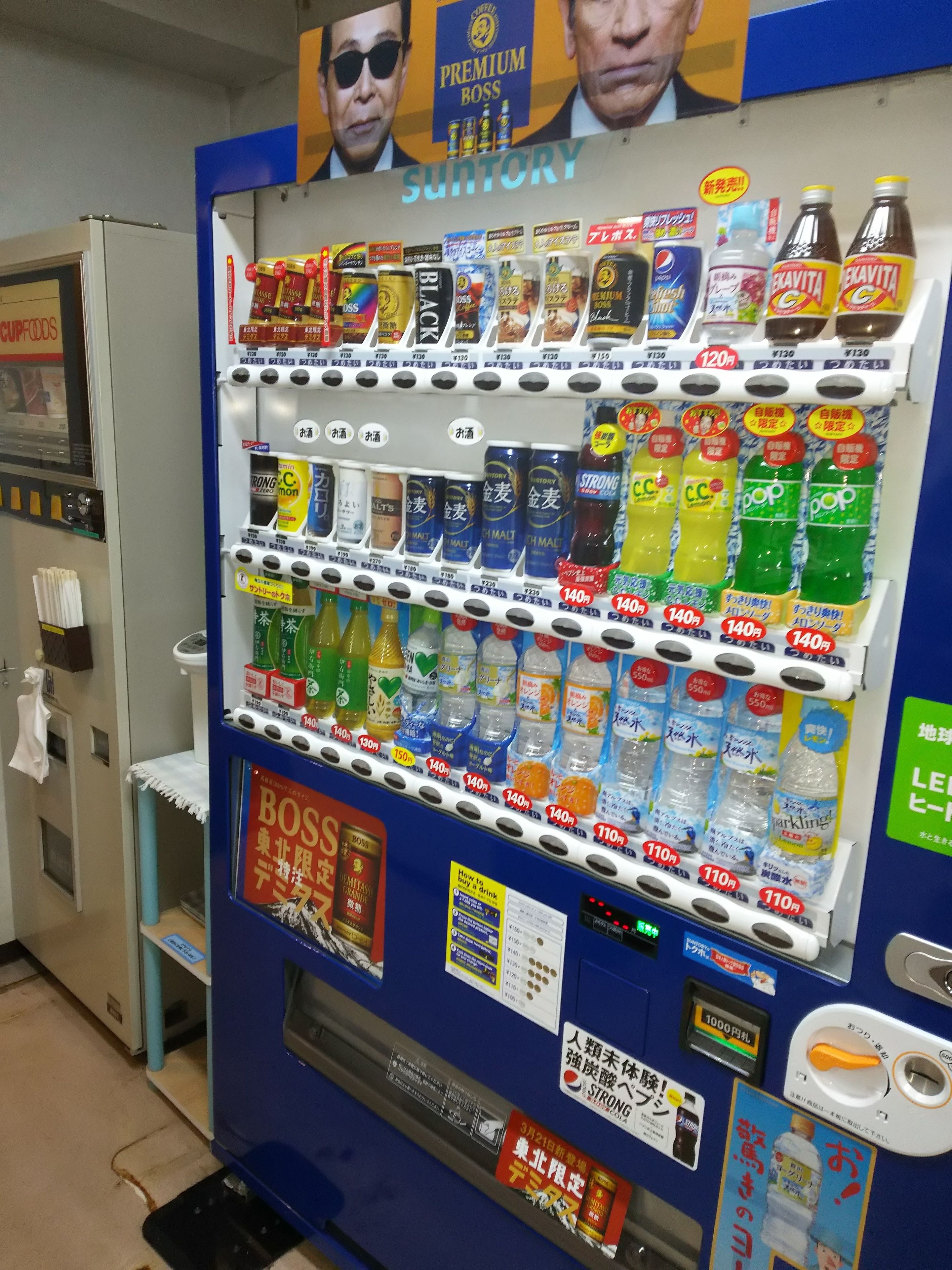 Máquina expendedora con diversas bebidas y aperitivos, incluyendo botellas de agua, refrescos y otras opciones.