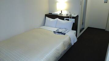 A hotel room with a single bed, a bedside table with a lamp, a phone, and a small table with a notepad and pen.