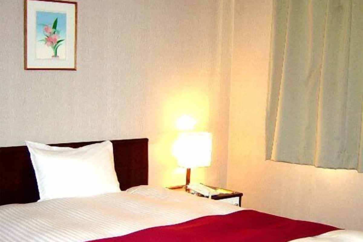 Ein Hotelzimmer mit einem Bett, einem Nachttisch, einer Lampe und einem gerahmten Bild an der Wand.