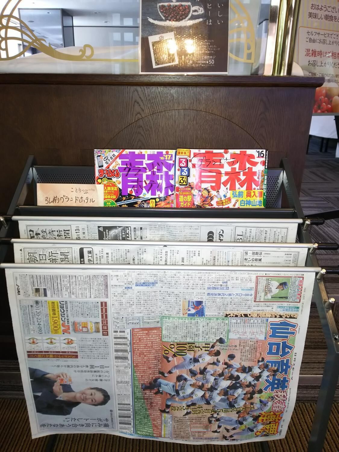 A display of Japanese newspapers and magazines with a coffee advertisement above.
