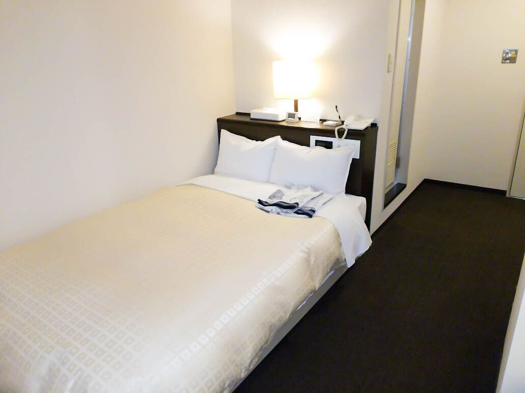 Una habitación de hotel con una cama, una mesita de noche con lámpara y un teléfono.