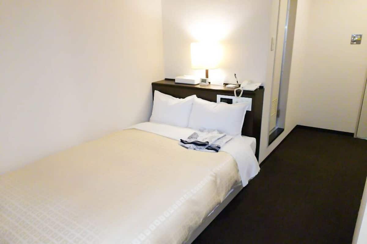 Ein Hotelzimmer mit einem Bett, einem Nachttisch mit Lampe und einem Telefon.