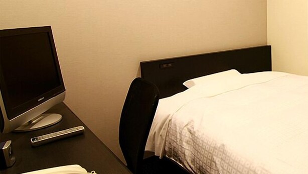A hotel room with a bed, a desk with a computer and a remote control, and a window with curtains. - Mito Riverside Hotel (Mito)