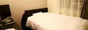 Une chambre d’hôtel avec un lit, un bureau équipé d’un ordinateur et d’une télécommande, et une fenêtre avec des rideaux.