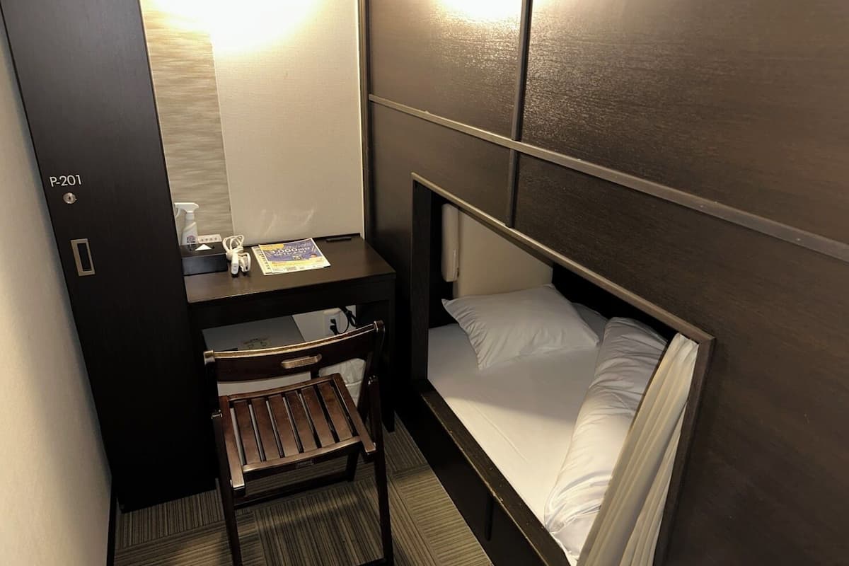 Una habitación de hotel compacta con una cama individual, un escritorio pequeño con una silla y una mesita de noche.