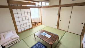 A traditional Japanese room with tatami flooring, a low wooden table, a futon bed, sliding doors, and a window with curtains. - Hotel CROWN HILLS MIYOSHI (Miyoshi)