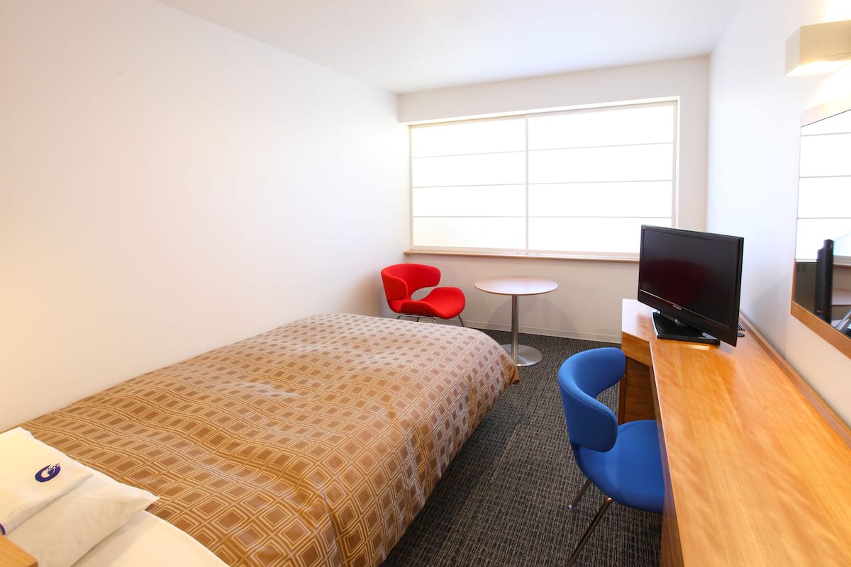 Una habitación de hotel con una cama, un escritorio con televisión, una silla roja y una mesa redonda pequeña.