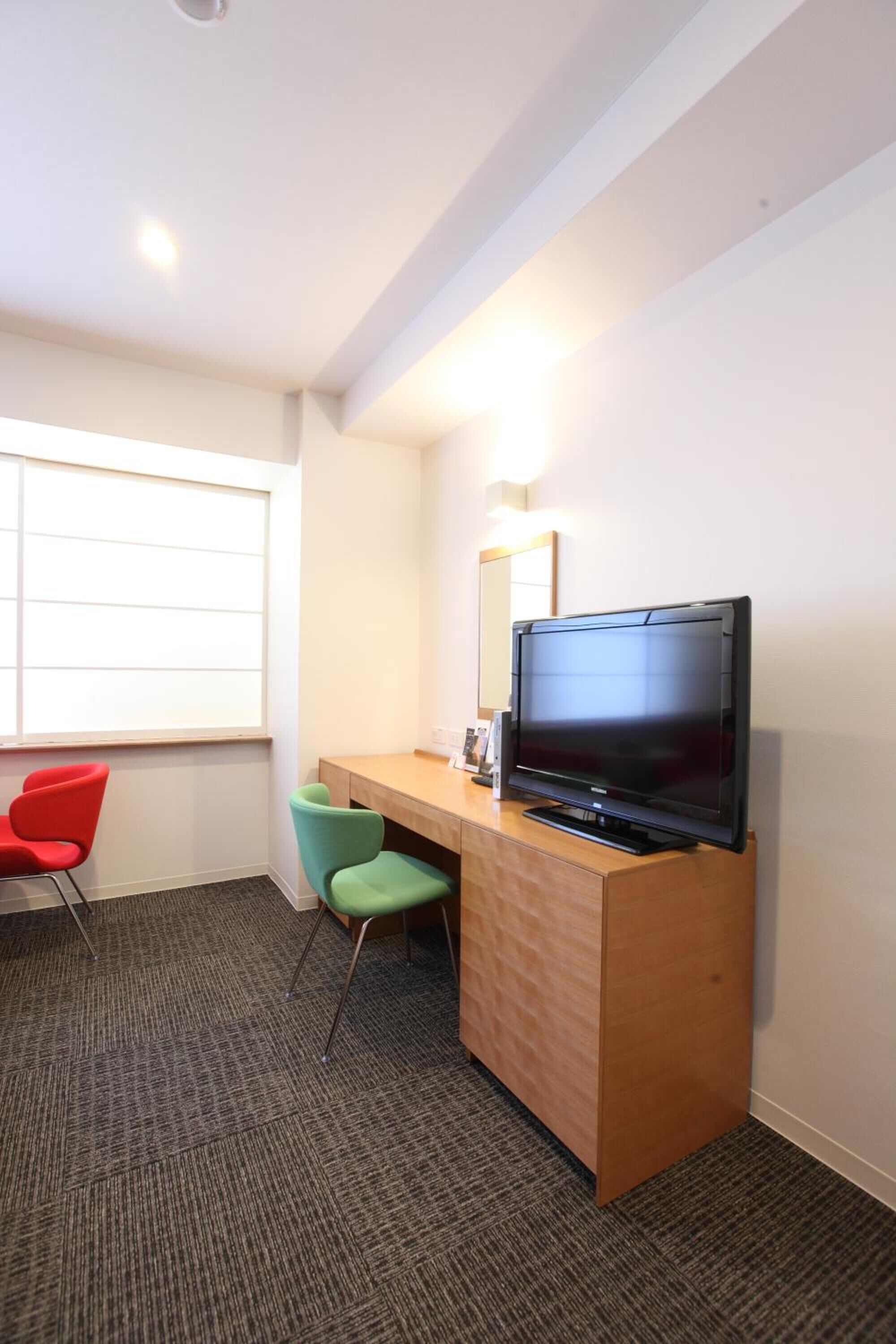 A hotel room with a wooden desk, a flat-screen TV, two chairs, and a large window.