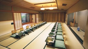 A traditional tatami mat room with a long table and chairs, a shoji screen, and a view of the outdoors. - Nagaoka Grand Hotel (Nagaoka)