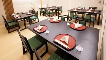 Comedor con varias mesas dispuestas, manteles individuales rojos, servilletas blancas y sillas con cojines verdes.