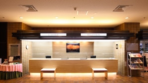 A reception area with a wooden counter, two receptionists' stations, a bench, and a magazine rack. - Nagaoka Grand Hotel (Nagaoka)