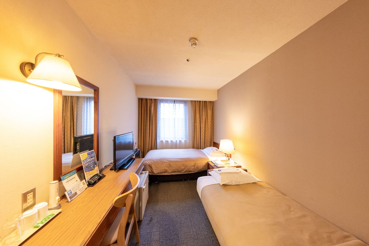 Una habitación de hotel con escritorio, dos camas, televisión y ventana con cortinas.