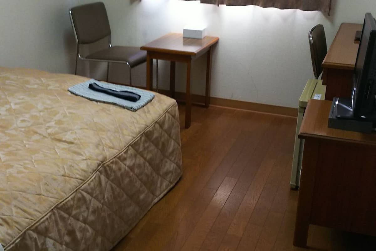 Ett hotellrum med en säng, ett skrivbord, en stol, ett litet bord och ett fönster med gardiner.