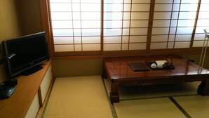 Una habitación tradicional japonesa con suelo de tatami, televisor, mesa de madera con bandeja y puertas correderas shoji.