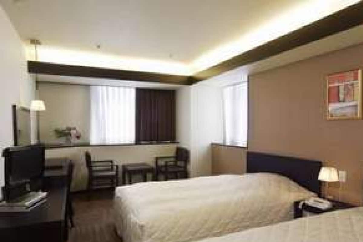 A hotel room with two beds, a desk, a chair, and a window.
