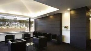 A modern hotel lobby with a seating area, a large window with a view, and a dark-colored reception desk.